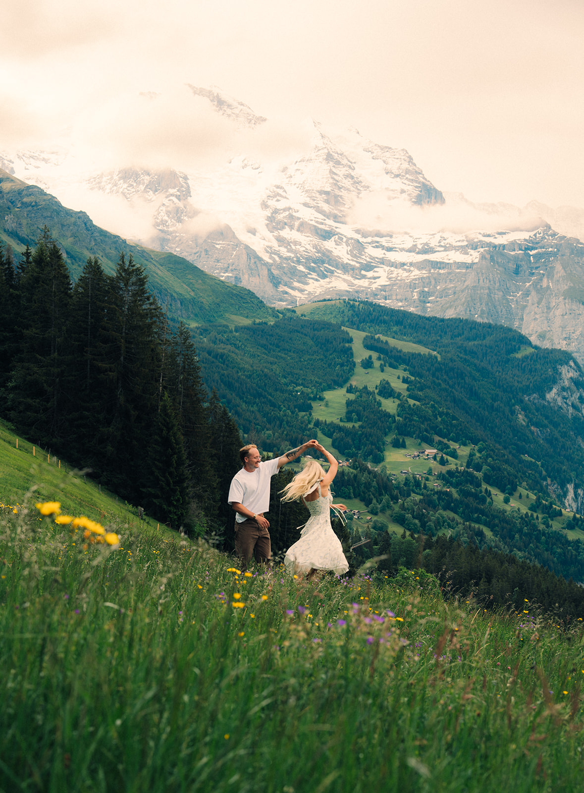 A cinematic photo of a couple posing near Wengen, Switzerland with the Swiss Alps in the background.