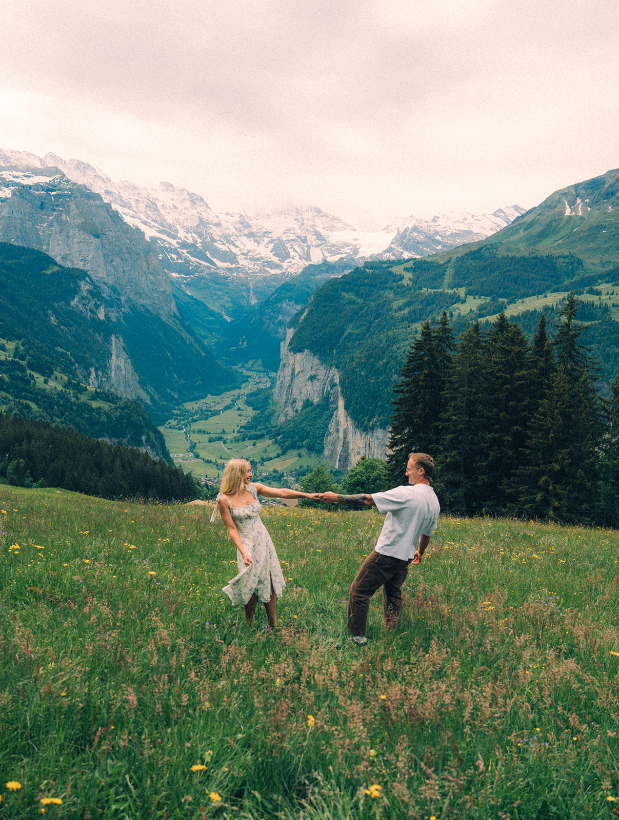 A cinematic photo of a couple posing near Wengen, Switzerland with the Swiss Alps in the background.