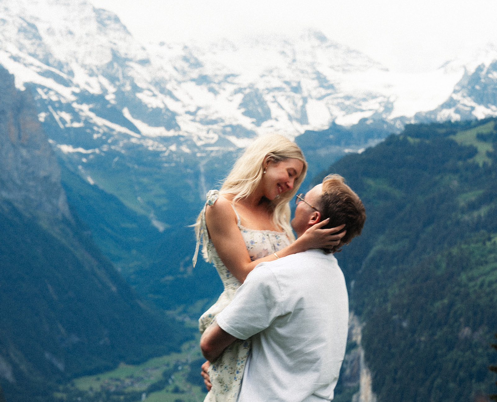 A cinematic photo of a couple posing near Wengen, Switzerland with the Swiss Alps in the background.
