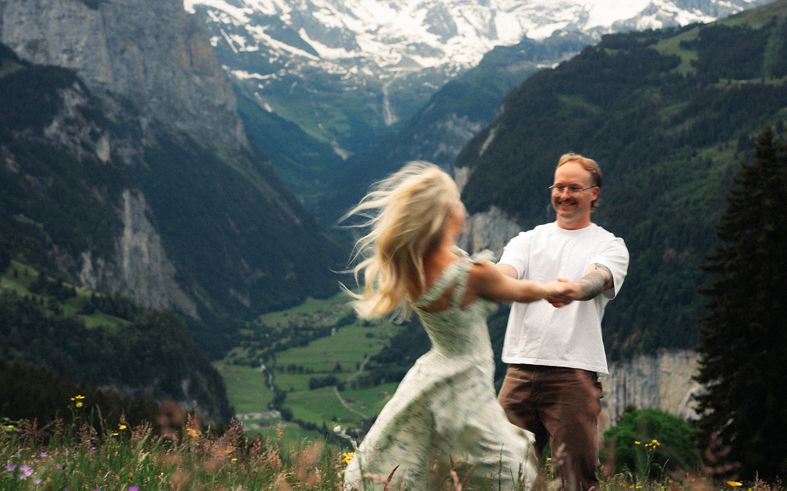 A cinematic photo of a couple posing near Wengen, Switzerland with the Swiss Alps in the background.