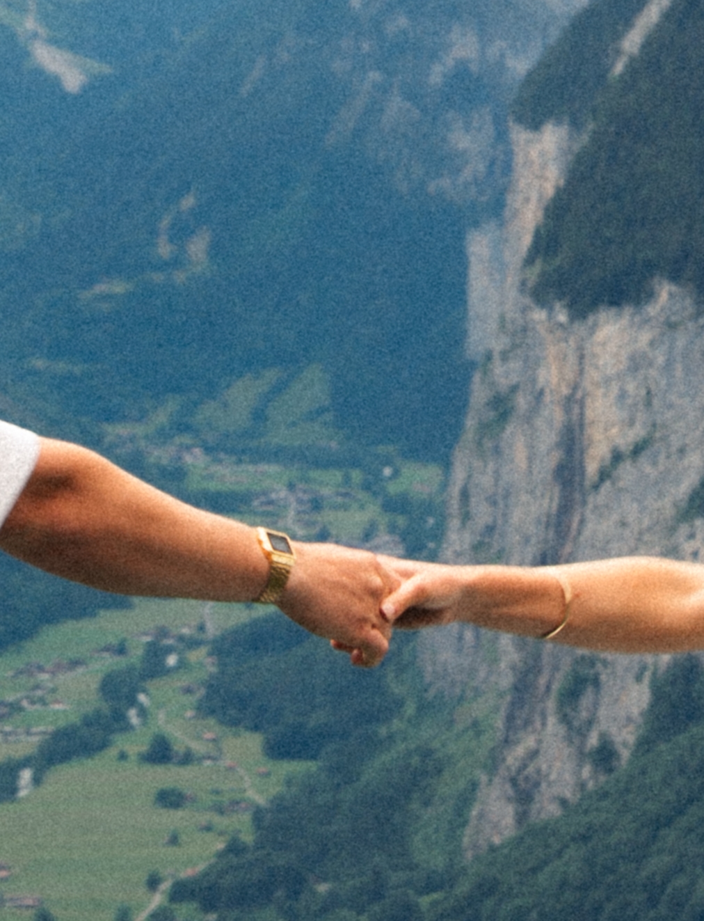 A cinematic detail shot of a couple's hands with the Swiss Alps in the background.