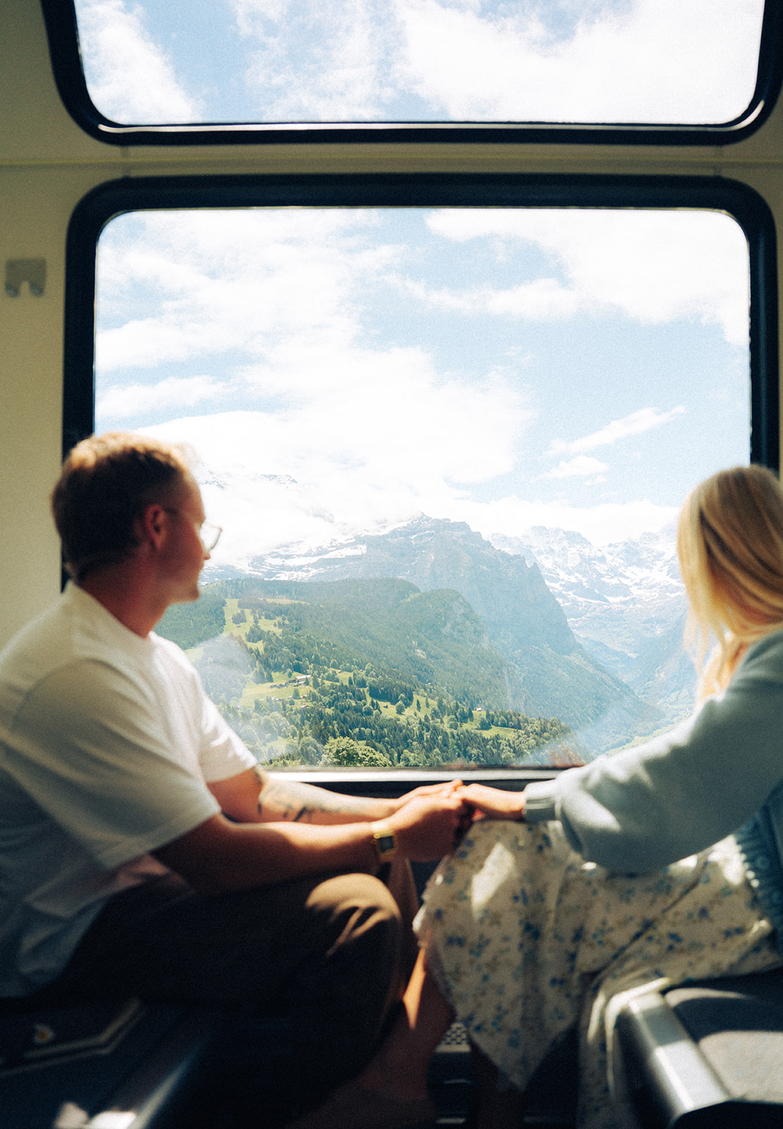 A cinematic photo of a couple in a train with the Swiss alps in the background.