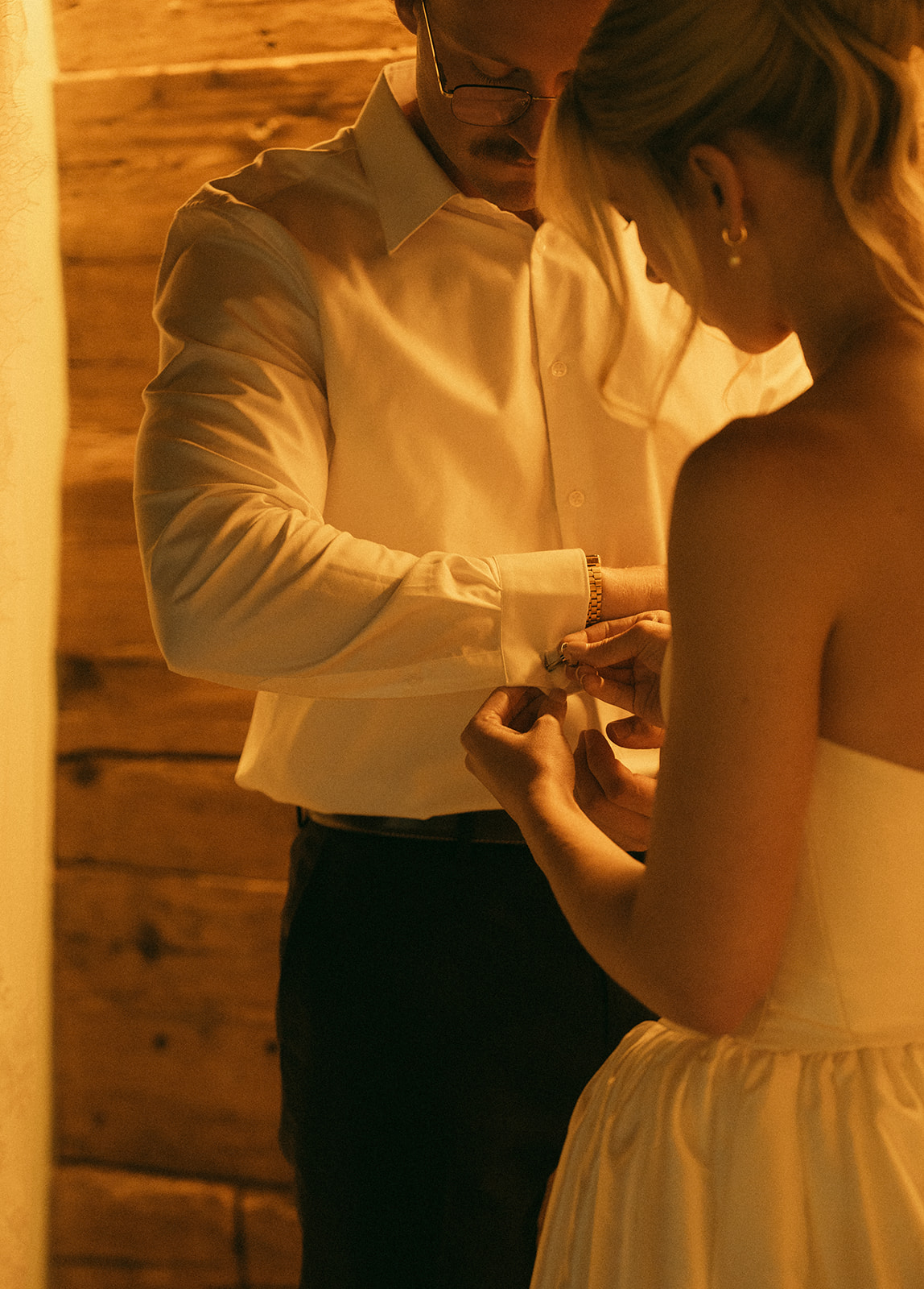 A cinematic photo of a bride helping the bridegroom fix his cuff links in their cabin in Innertkirchen, Switzerland for their elopement.