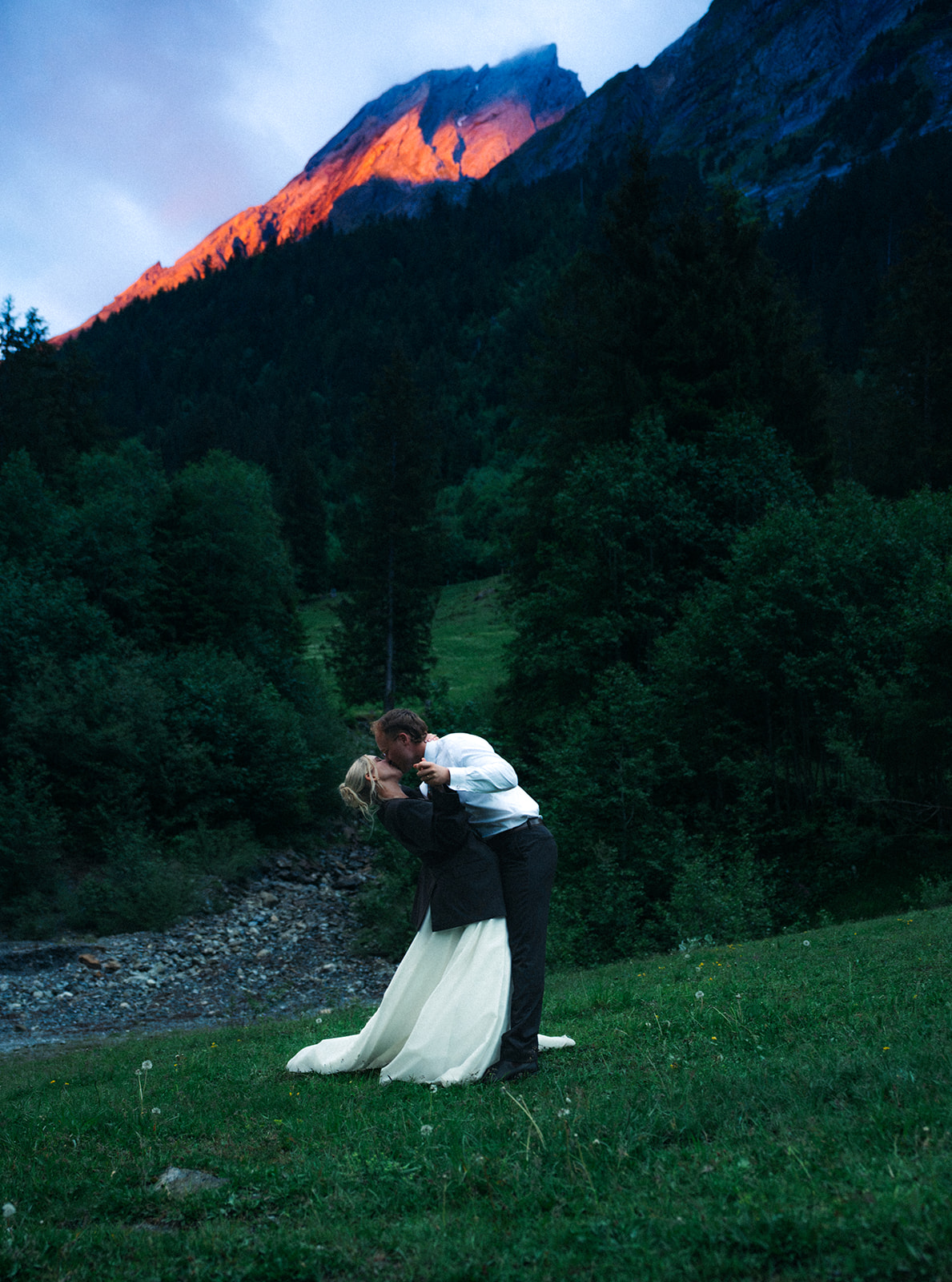 A cinematic photo of a bride and bridegroom during their elopement in Rosenlaui, Switzerland with the Swiss alps in the background. The mountains have Alpenglow on them.